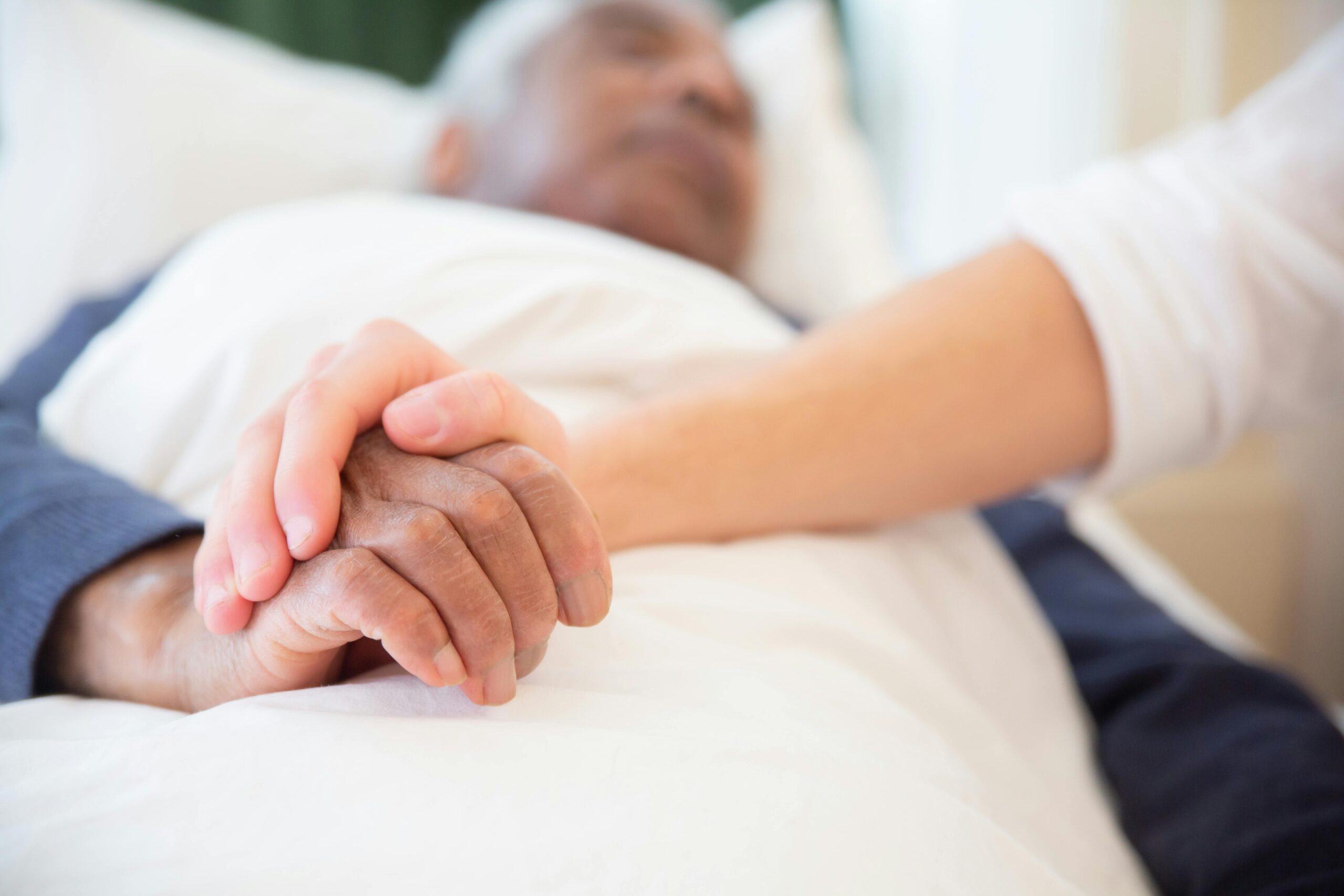 Hands holding on a man's deathbed