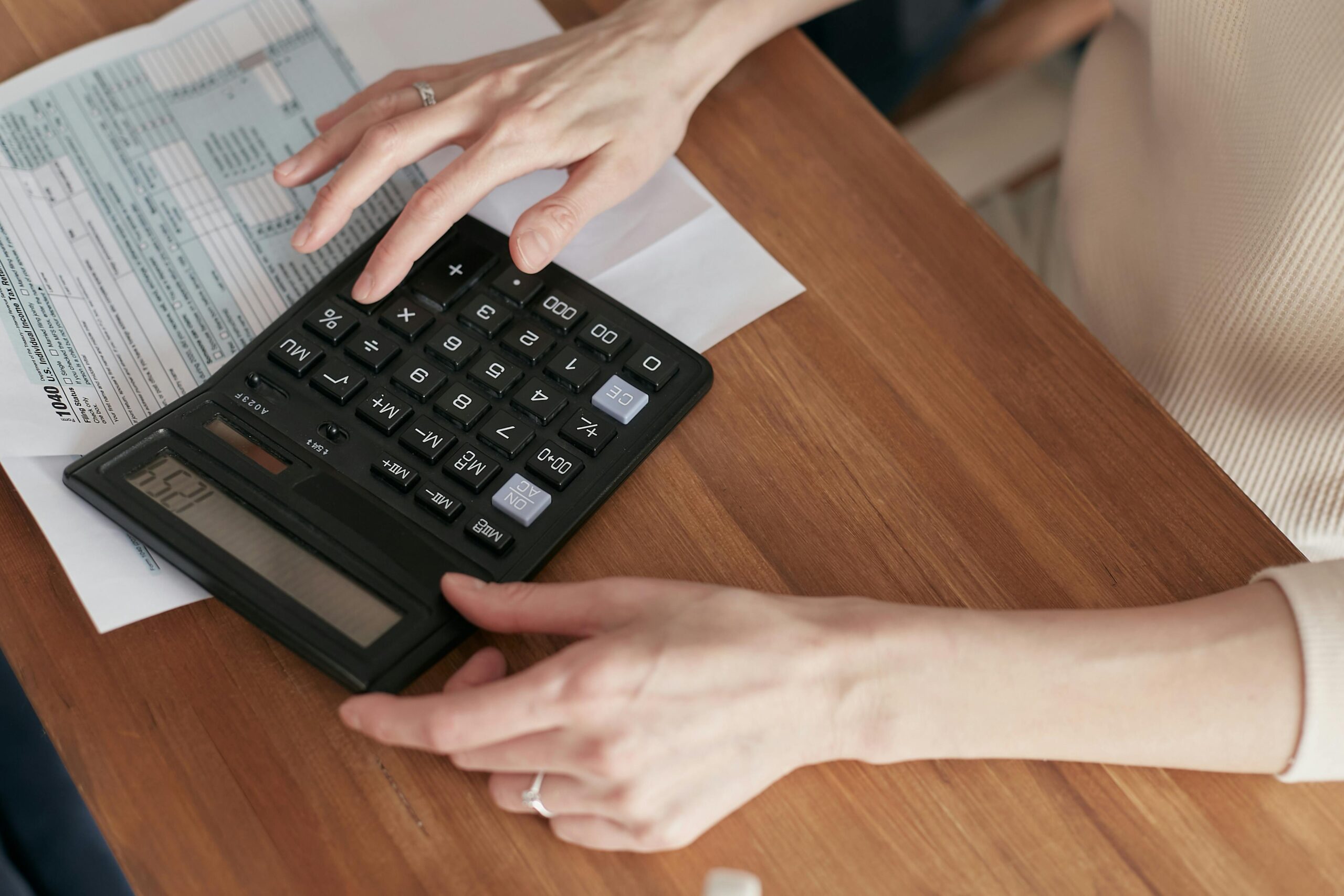 Woman's hands typing into a calculator atop an tax form